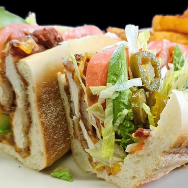 A large American sub sandwich, cut in half, filled with chicken, bacon, lettuce, tomato, and jalapeños.
