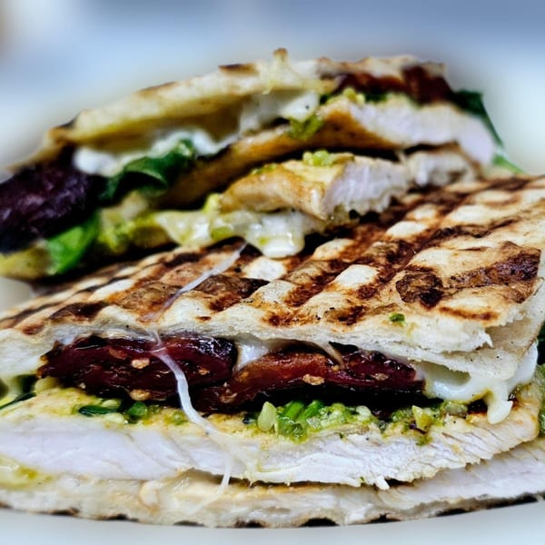 Close-up of a grilled chicken panini with pesto, sun-dried tomatoes, and melted cheese.