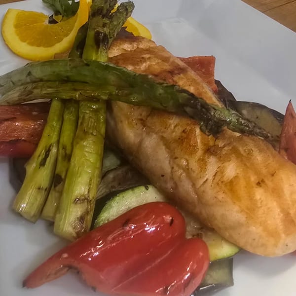 Grilled salmon with asparagus, red bell peppers, zucchini, and orange slices on a white plate.