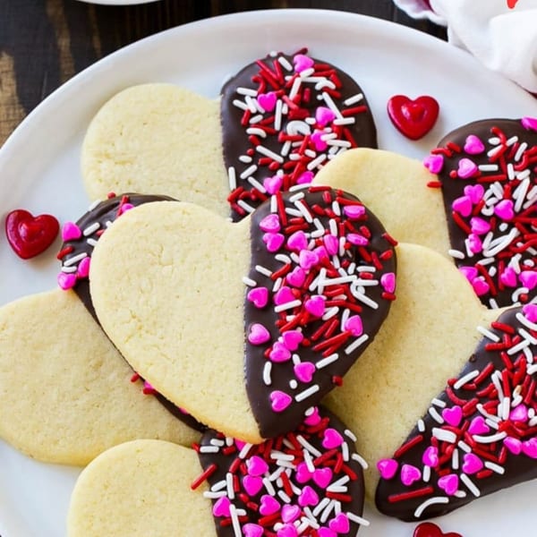 Heart-shaped sugar cookies, half-dipped in chocolate and covered with red, white, and pink sprinkles.