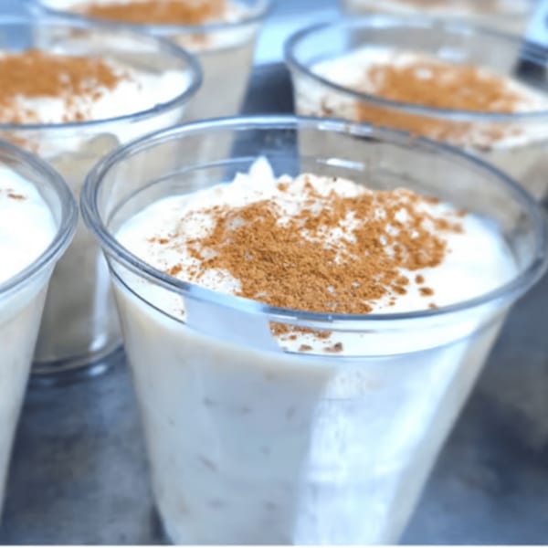 Several clear cups of rice pudding with cinnamon sprinkled on top, ready to be served.