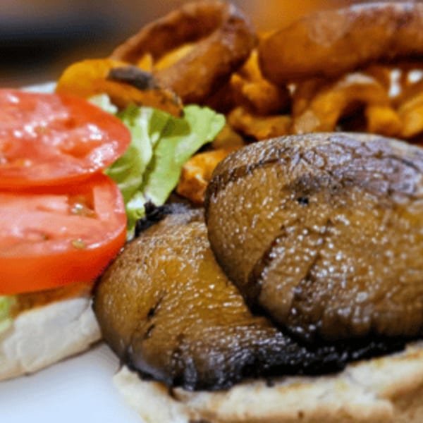 A grilled mushroom burger with lettuce, tomato, and a side of onion rings and sweet potato fries.