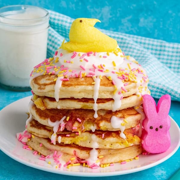Stack of pancakes with white icing, pink and yellow sprinkles, topped with a yellow Peep, and a pink Peep on the side.