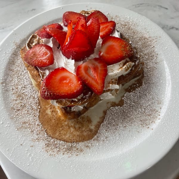 French toast topped with whipped cream, fresh strawberries, powdered sugar, and cinnamon on a white plate.